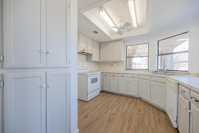 kitchen with a tray ceiling, light countertops, a sink, white appliances, and under cabinet range hood