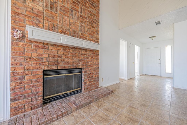 unfurnished living room with a textured ceiling, a fireplace, visible vents, and baseboards