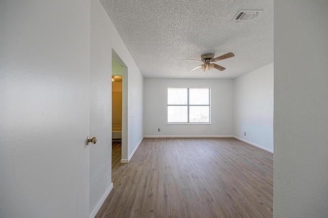 empty room with visible vents, ceiling fan, a textured ceiling, wood finished floors, and baseboards