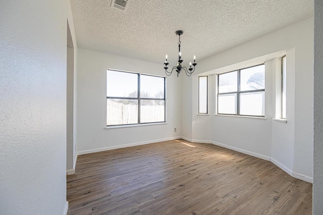 spare room featuring baseboards, a notable chandelier, visible vents, and wood finished floors