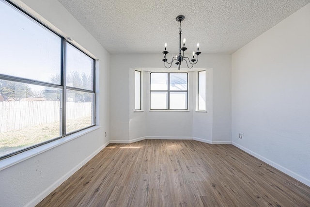 unfurnished room with a notable chandelier, a textured ceiling, baseboards, and wood finished floors