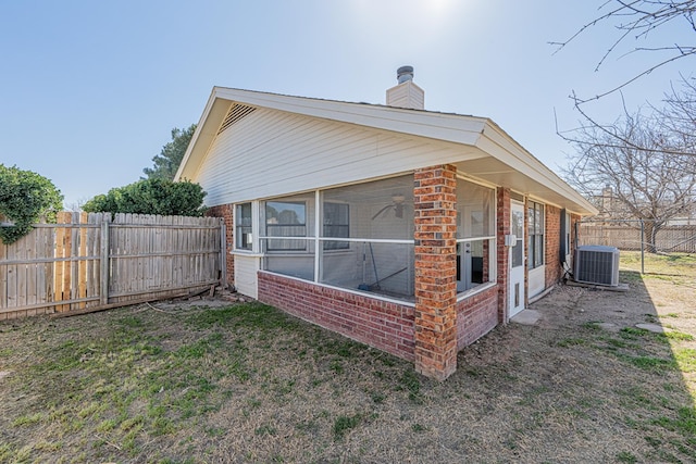 view of property exterior with brick siding, a chimney, central AC unit, a sunroom, and a fenced backyard