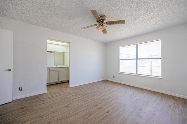 spare room featuring a textured ceiling, wood finished floors, a ceiling fan, and baseboards