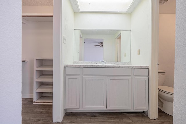 bathroom featuring toilet, a skylight, wood finished floors, vanity, and baseboards