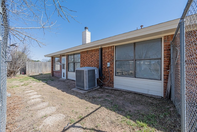 rear view of house featuring a chimney, central AC unit, fence, and brick siding