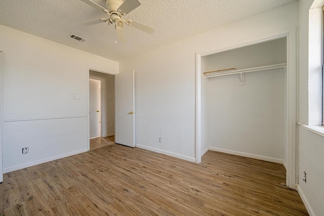 unfurnished bedroom with a textured ceiling, wood finished floors, visible vents, baseboards, and a closet