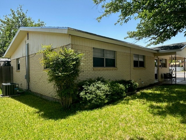 view of side of property featuring a yard, central AC, and brick siding