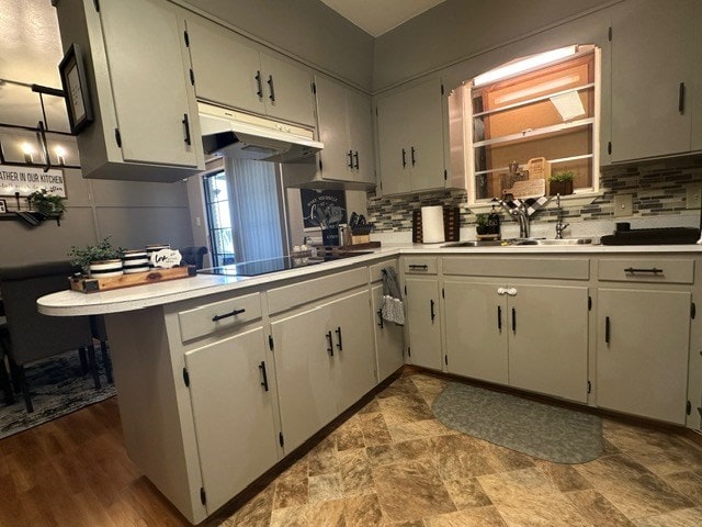 kitchen with black electric stovetop, under cabinet range hood, a peninsula, light countertops, and backsplash