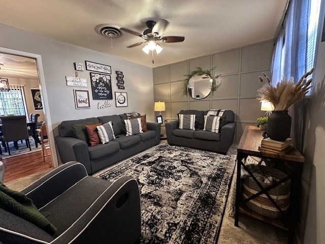 living room with ceiling fan with notable chandelier, visible vents, and a decorative wall