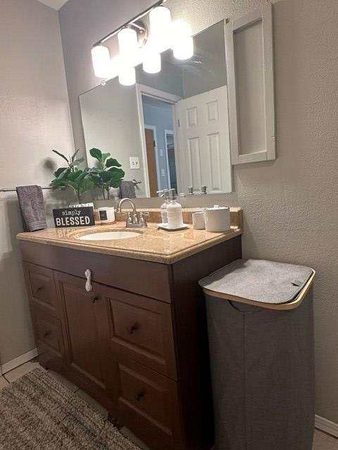 bathroom with a textured wall, tile patterned flooring, baseboards, and vanity