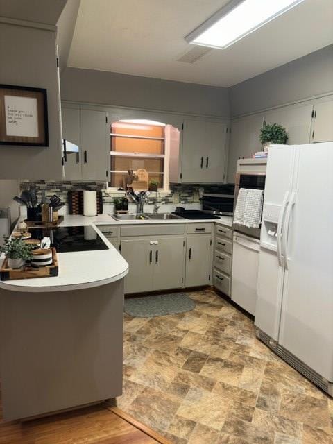 kitchen featuring gray cabinets, light countertops, under cabinet range hood, white fridge with ice dispenser, and a sink