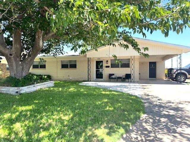 single story home featuring driveway, a front lawn, an attached carport, and brick siding