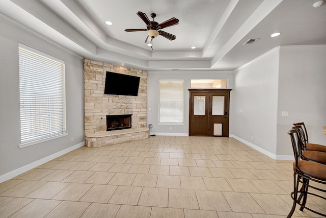 entrance foyer featuring ceiling fan, a fireplace, visible vents, a raised ceiling, and baseboards