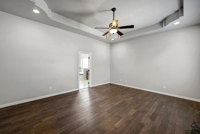 empty room with a raised ceiling, dark wood-type flooring, baseboards, and a ceiling fan