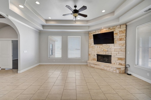 unfurnished living room featuring a fireplace, light tile patterned floors, a raised ceiling, arched walkways, and ceiling fan