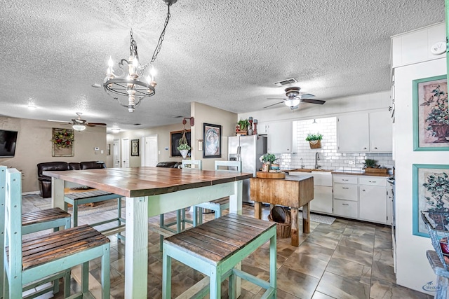 1412 Sparks St, Midland, TX 79701 - kitchen with a ceiling fan, white cabinets, a chandelier, stainless steel fridge, and a textured ceiling