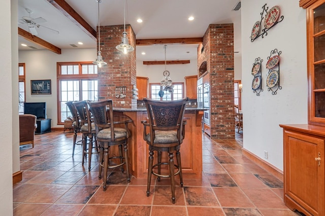 bar featuring ceiling fan, hanging light fixtures, beamed ceiling, brick wall, and dark stone counters