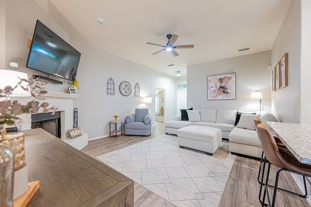 living area with ceiling fan, a fireplace, light wood-style floors, and baseboards