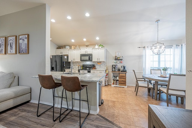 kitchen featuring black appliances, backsplash, a breakfast bar area, white cabinets, and a chandelier