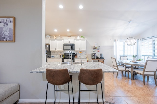 kitchen with black microwave, a sink, a kitchen breakfast bar, a chandelier, and decorative backsplash