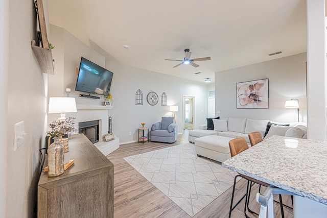 living room featuring a fireplace, a ceiling fan, light wood-type flooring, and baseboards