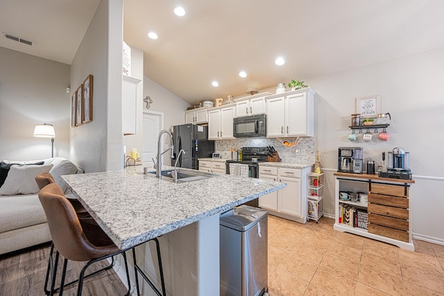 kitchen featuring black appliances, vaulted ceiling, a sink, tasteful backsplash, and a breakfast bar area