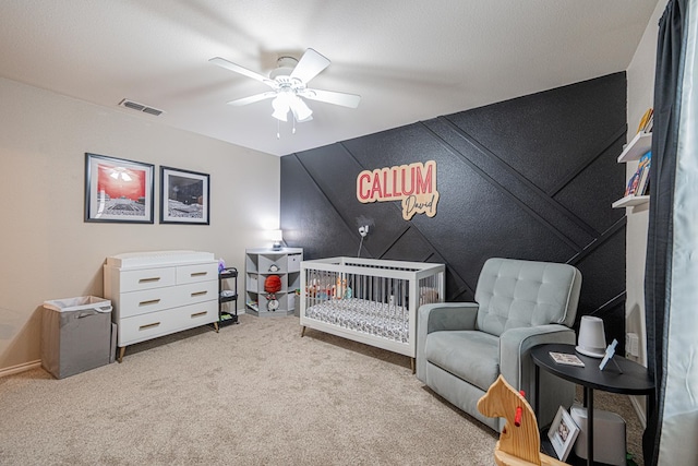 carpeted bedroom with ceiling fan and a nursery area