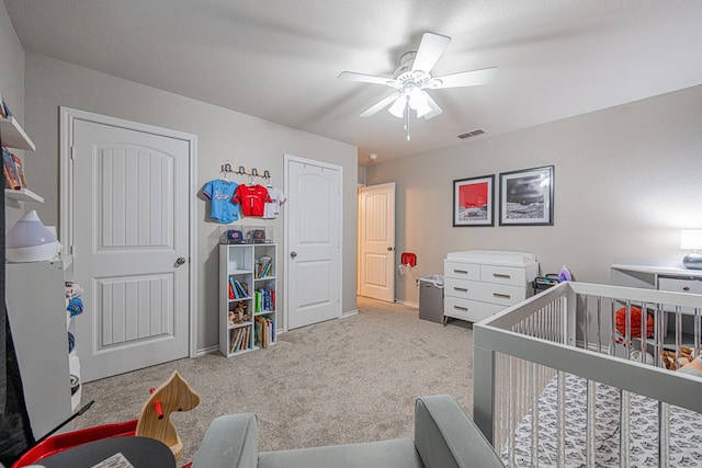 carpeted bedroom featuring a crib, baseboards, and a ceiling fan
