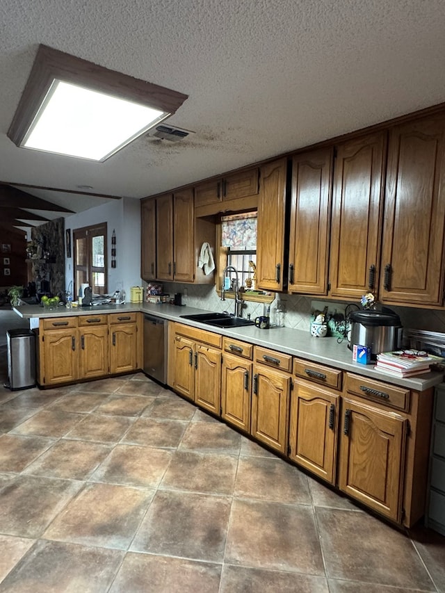 kitchen featuring a sink, a textured ceiling, brown cabinetry, stainless steel dishwasher, and visible vents