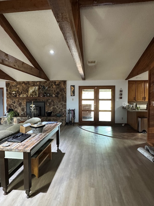 living area featuring french doors, a stone fireplace, visible vents, beam ceiling, and wood finished floors
