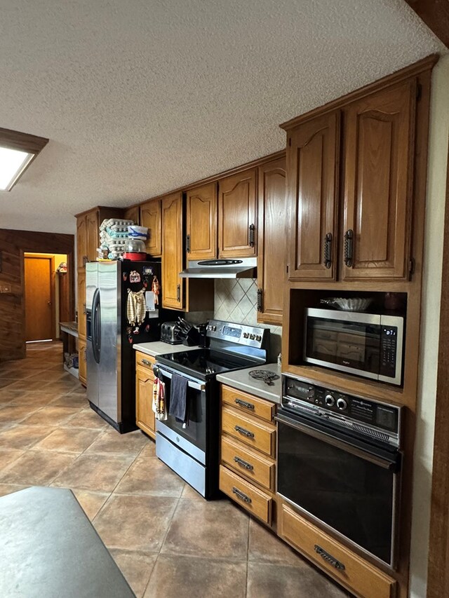 kitchen featuring decorative backsplash, light countertops, a textured ceiling, under cabinet range hood, and stainless steel appliances