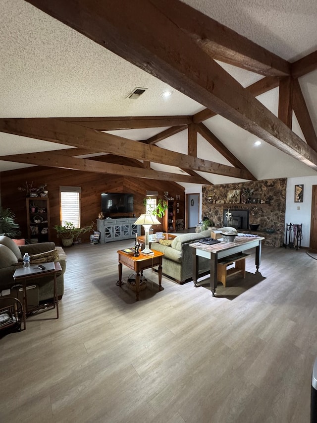 living area with lofted ceiling with beams, a textured ceiling, wood walls, wood finished floors, and visible vents