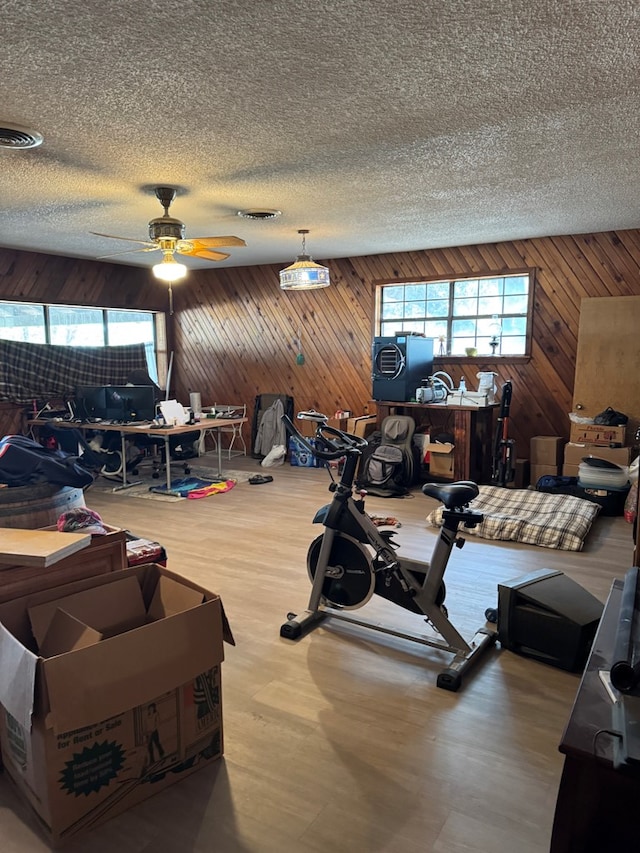 living room with wooden walls, ceiling fan, a textured ceiling, and visible vents
