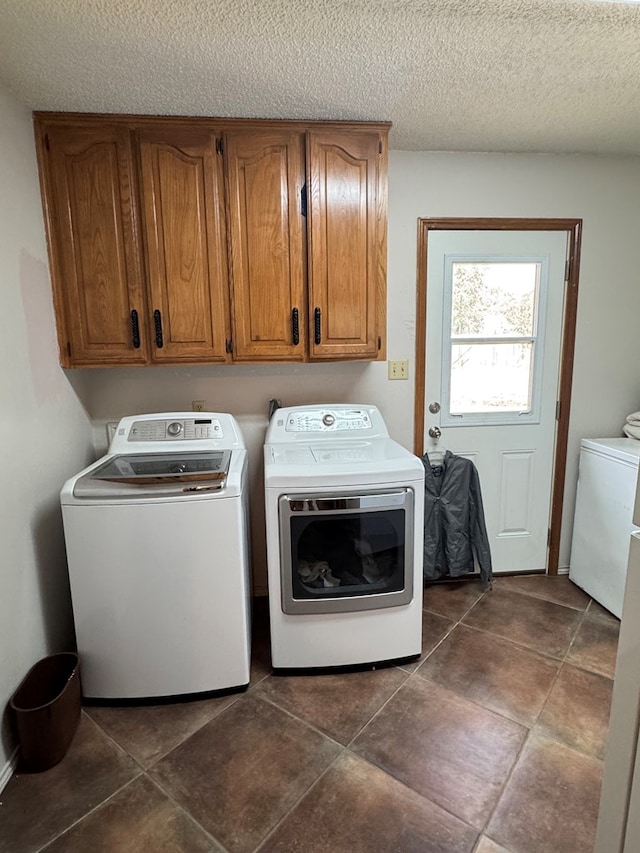 clothes washing area with separate washer and dryer, a textured ceiling, and cabinet space