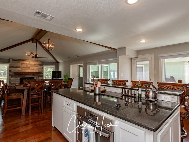 kitchen featuring a stone fireplace, visible vents, stainless steel oven, open floor plan, and white cabinets