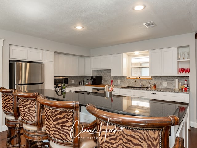 kitchen with stainless steel appliances, a sink, visible vents, white cabinets, and tasteful backsplash