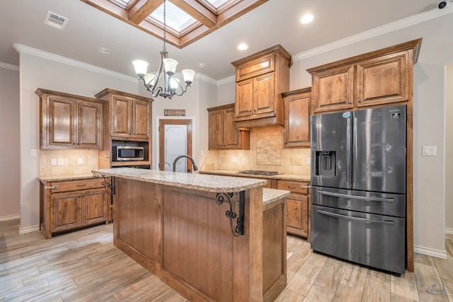 kitchen featuring a skylight, a center island with sink, stainless steel appliances, hanging light fixtures, and a chandelier