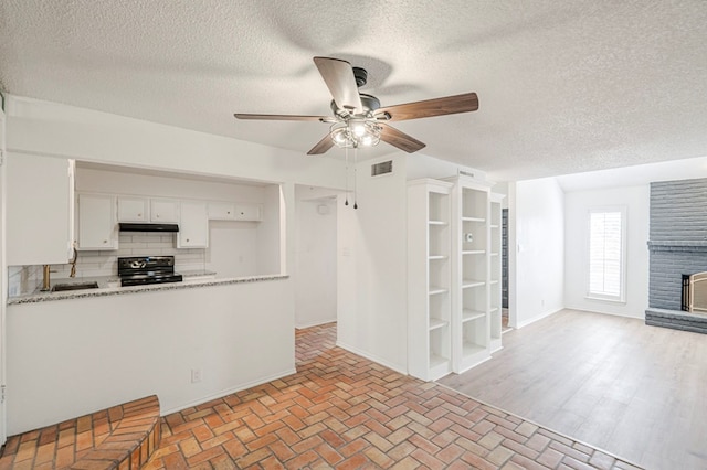 kitchen featuring visible vents, backsplash, a brick fireplace, white cabinets, and black / electric stove