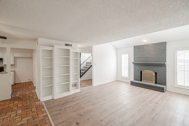 unfurnished living room featuring a fireplace, light wood finished floors, visible vents, stairway, and baseboards