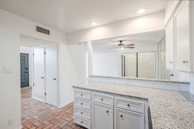 kitchen with brick floor, light stone counters, recessed lighting, visible vents, and white cabinetry