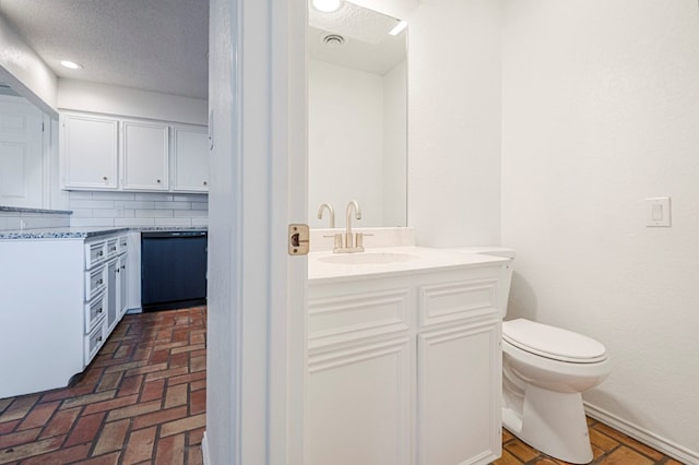 bathroom with brick floor, backsplash, toilet, a sink, and a textured ceiling