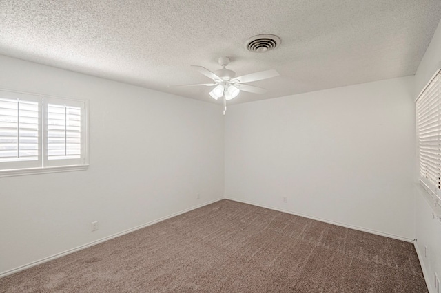 empty room with a ceiling fan, dark colored carpet, visible vents, and a textured ceiling