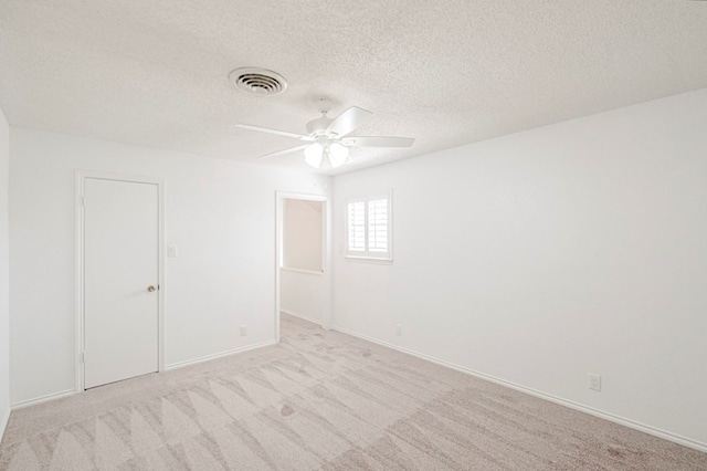 spare room with a textured ceiling, light carpet, visible vents, baseboards, and a ceiling fan