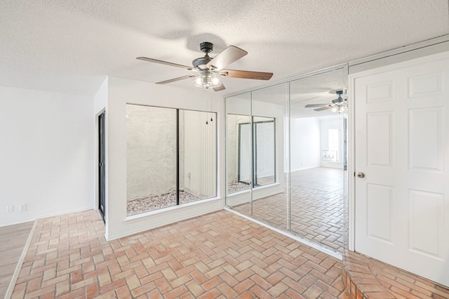 spare room featuring brick floor, ceiling fan, a textured ceiling, and baseboards