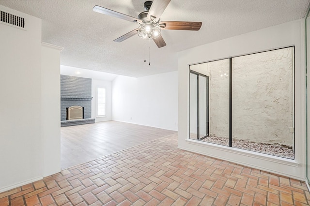 unfurnished living room with visible vents, ceiling fan, brick floor, a textured ceiling, and a fireplace