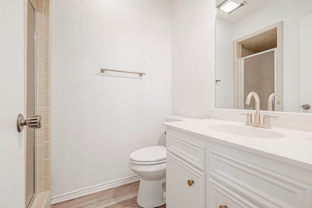 full bath with toilet, a tile shower, vanity, wood finished floors, and baseboards