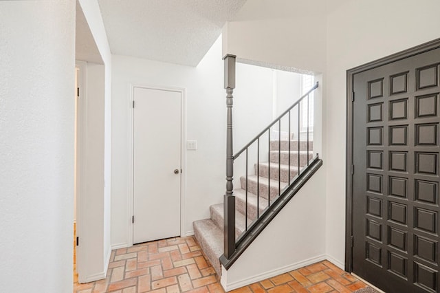 entrance foyer featuring brick floor, a textured ceiling, and stairs