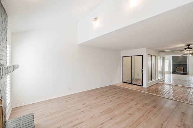 unfurnished living room with a large fireplace, light wood finished floors, baseboards, ceiling fan, and a textured ceiling