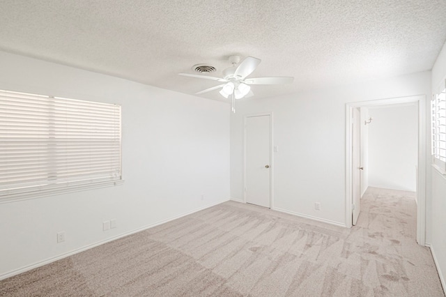 empty room featuring a textured ceiling, visible vents, and light colored carpet