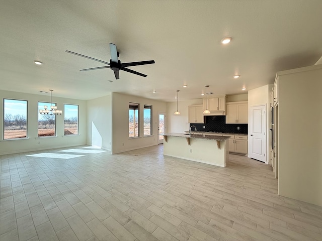 kitchen featuring a breakfast bar, a kitchen island with sink, open floor plan, and decorative backsplash